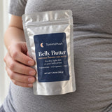 TummyHush Belly Butter pouch held in one hand against a grey shirt