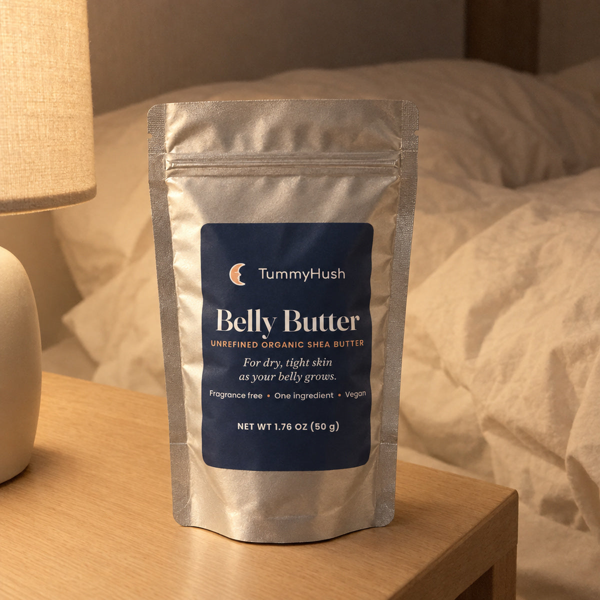 TummyHush Belly Butter pouch on a bedside table beside a lamp