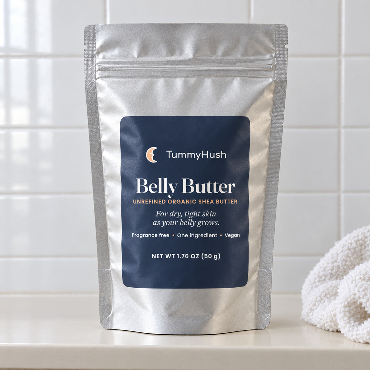 TummyHush Belly Butter pouch on a bathroom shelf beside a washcloth