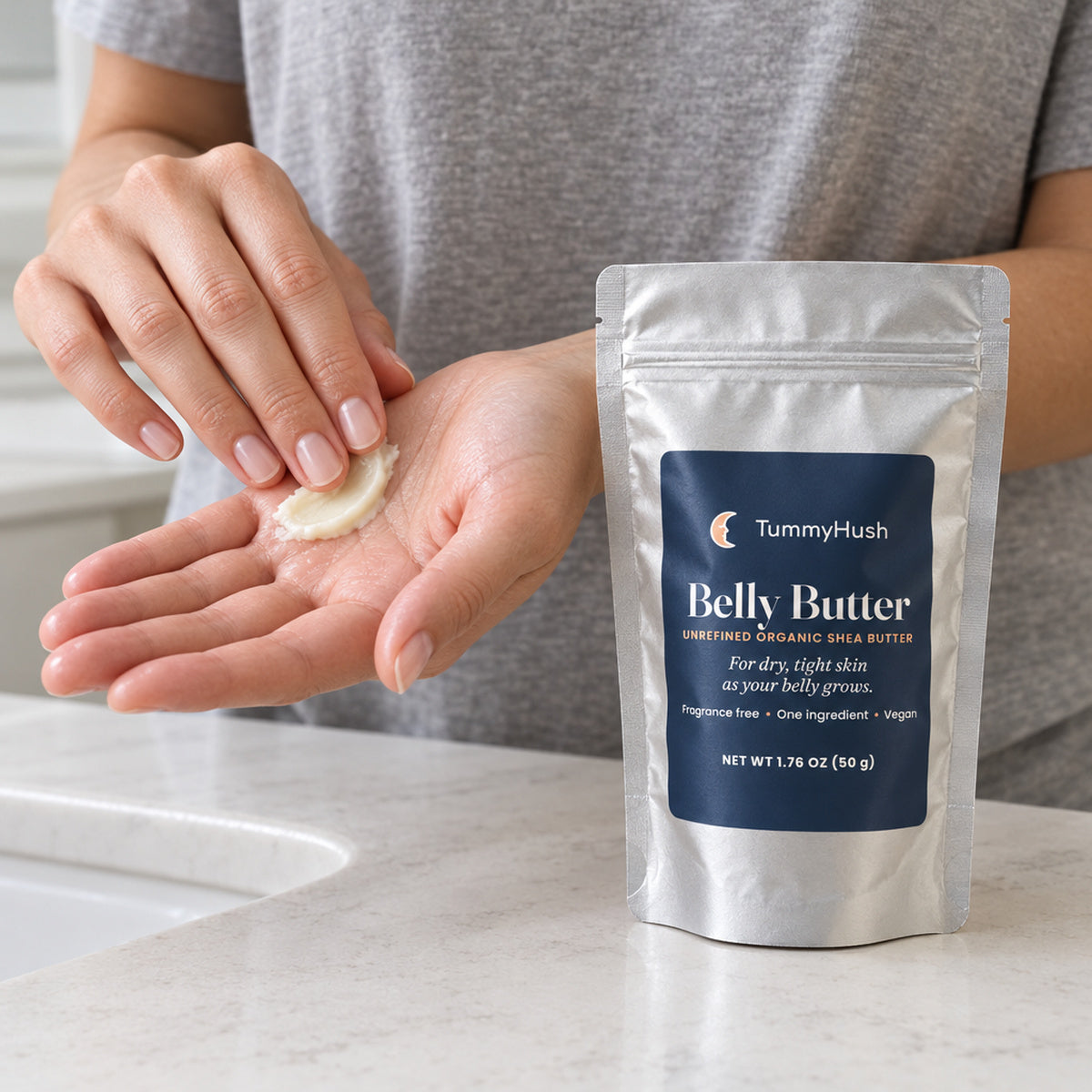 TummyHush Belly Butter pouch beside hands warming a smooth shea butter swipe