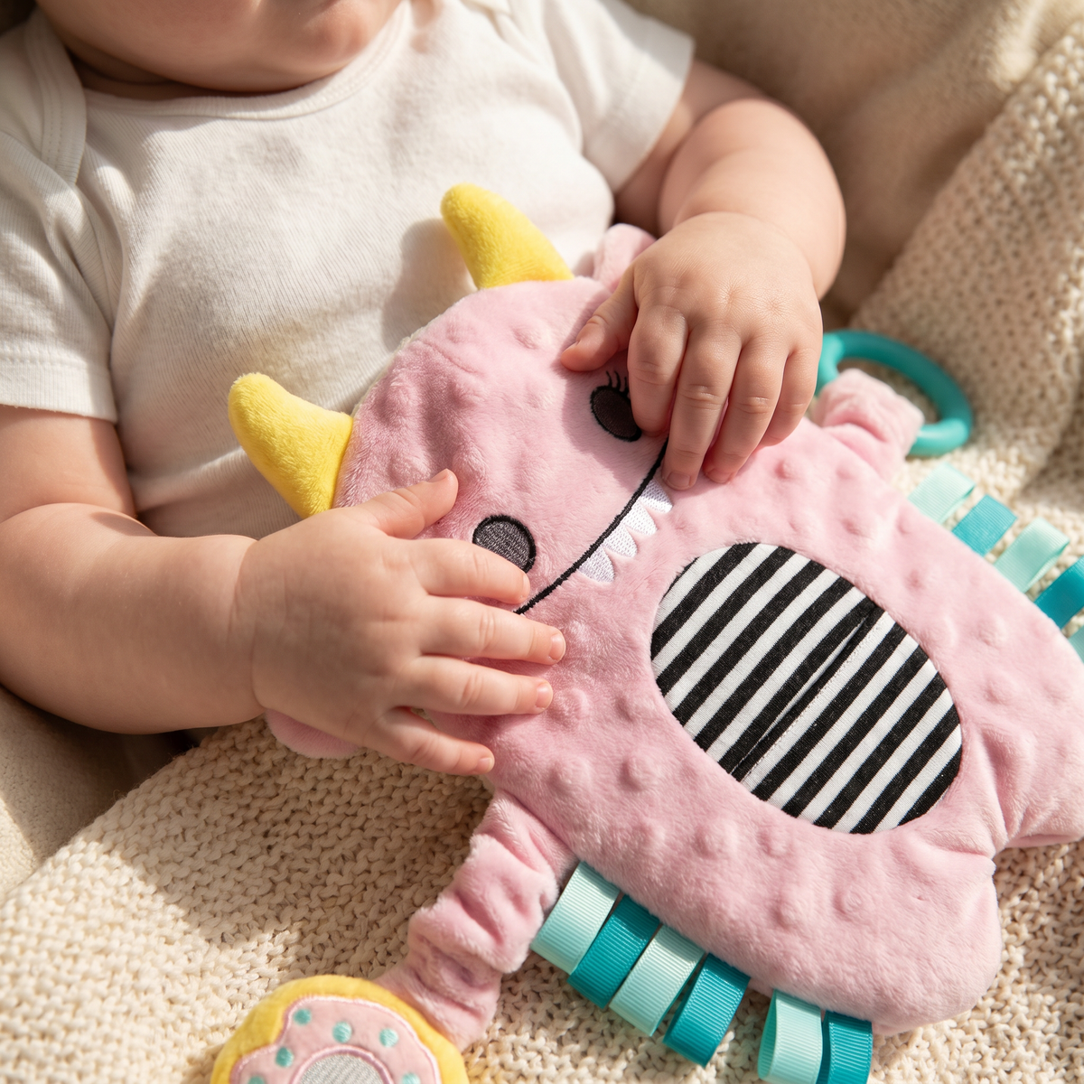 Close-up of a baby’s hands on the Snuggle Monster’s soft plush face and striped belly